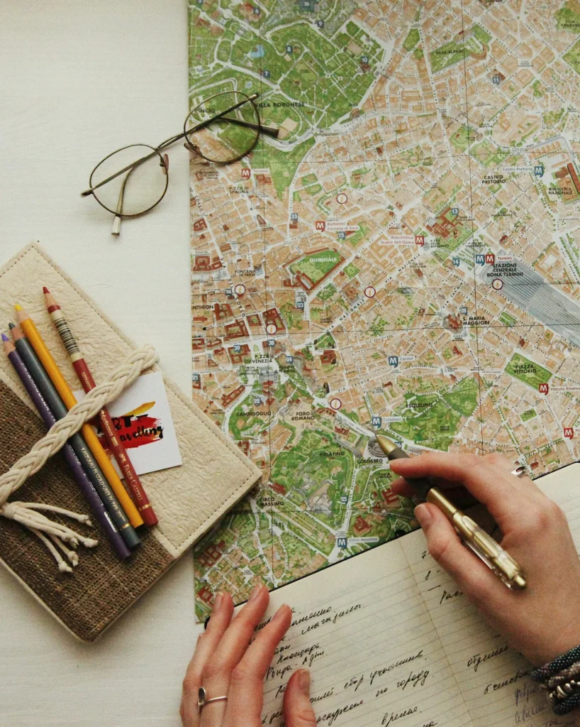 Hands planning a journey on a paper map beside a notebook and glasses