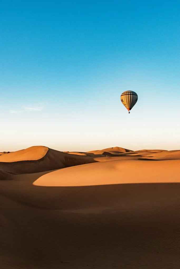 A hot-air balloon drifting above golden sand dunes