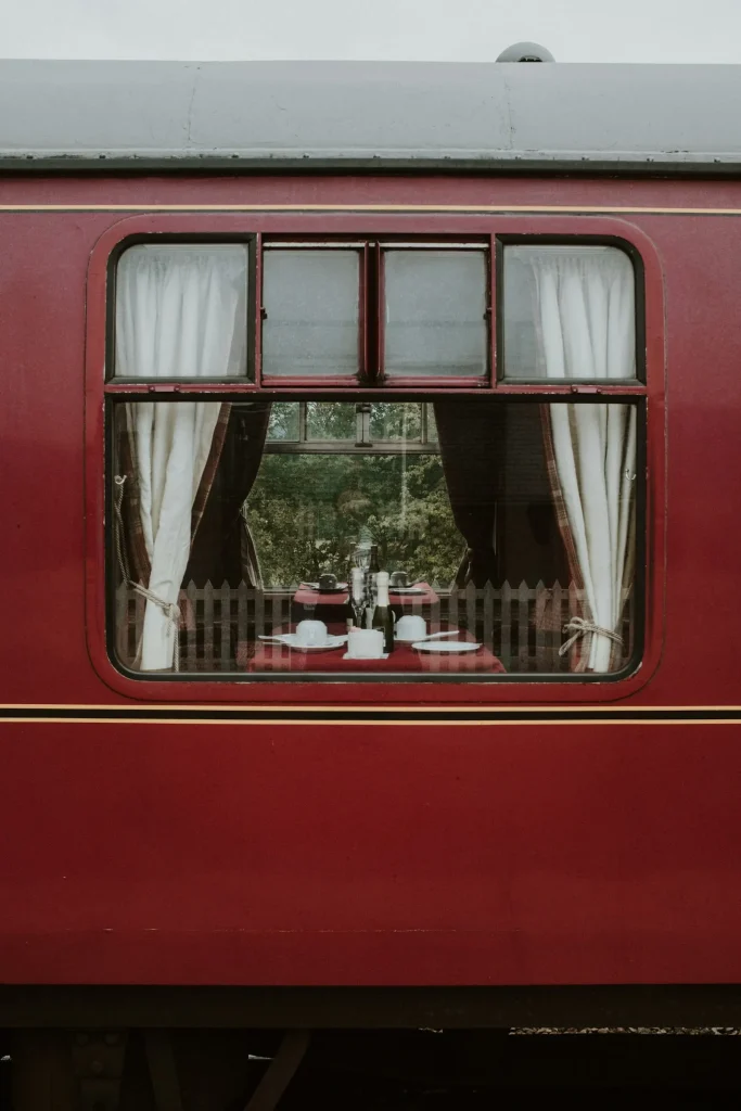 A vintage red train carriage with a dining table set inside the window