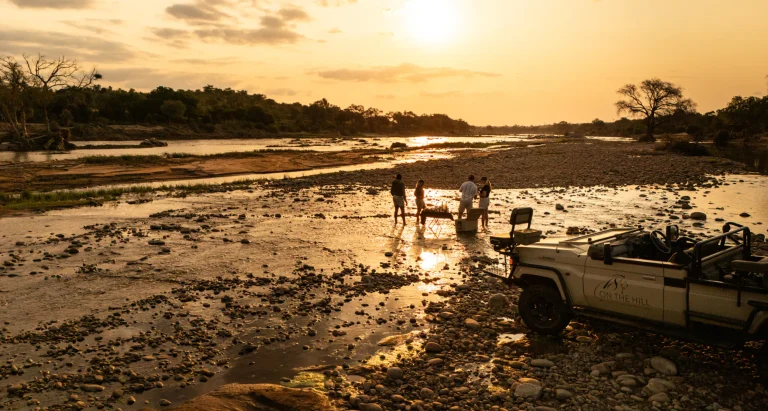 Guests at a riverbed stop during a safari at sunset