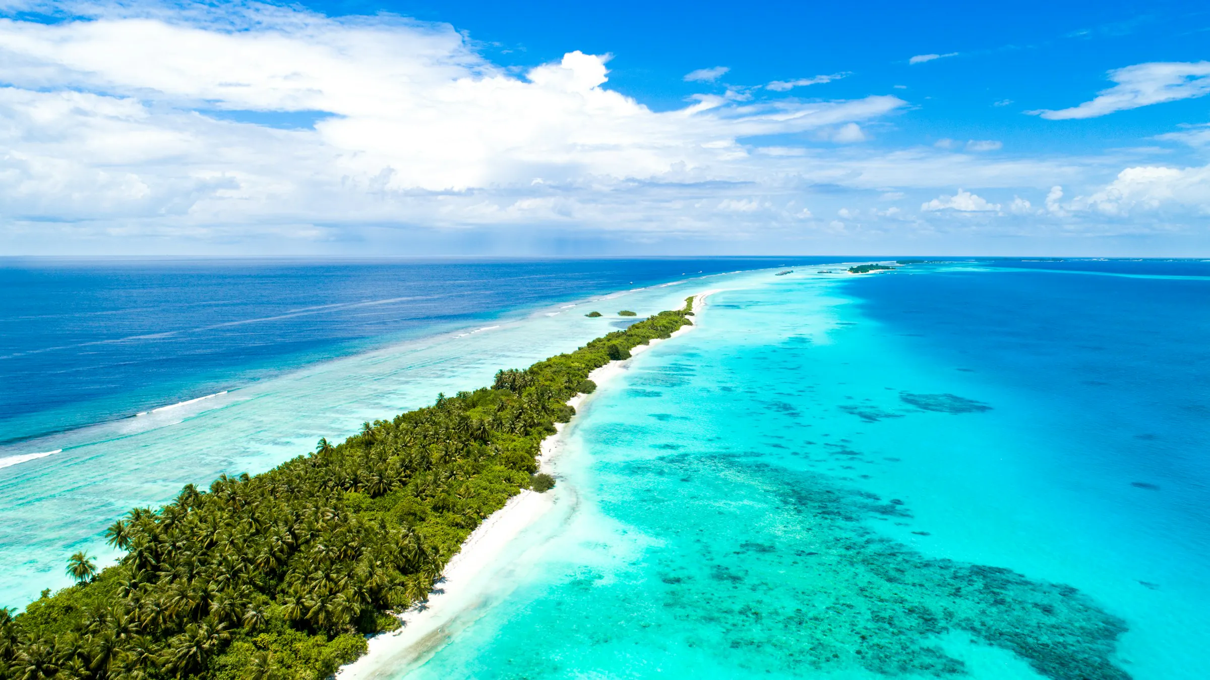 Aerial view of a palm-covered Maldives island edged by turquoise lagoon