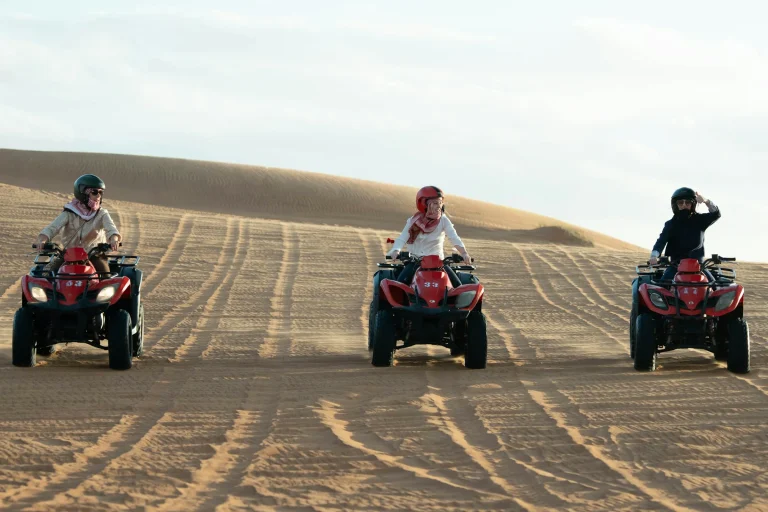 Three riders on quad bikes in the dunes