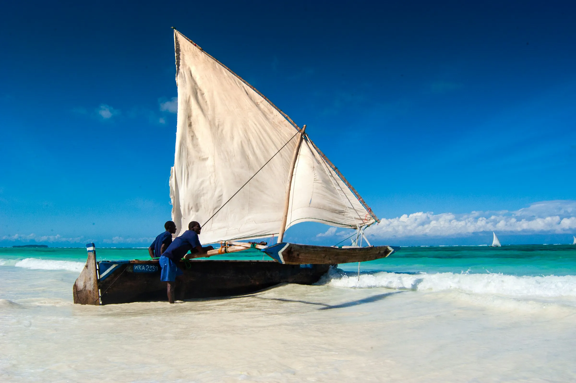 Fishermen launching a traditional dhow from a beach in Matemwe, Zanzibar